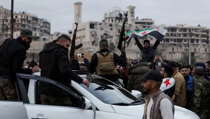 أشخاص يحتفلون بالقرب من قوات أمن سورية في حي الشيخ مقصود بمدينة حلب شمال غرب سوريا. 10 يناير 2026 - REUTERS