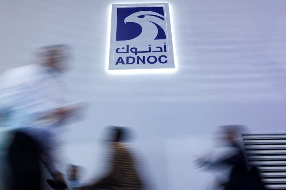 أشخاص يسيرون أمام شعار شركة بترول أبوظبي الوطنية (أدنوك) خلال معرض في أبوظبي يوم 3 نوفمبر 2025 - رويترز